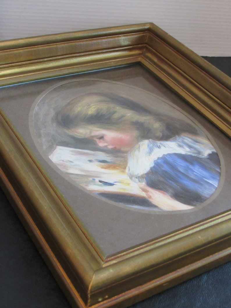 May include: A framed painting of a young girl with blonde hair, wearing a blue dress, reading a book. The painting is set in a gold frame.