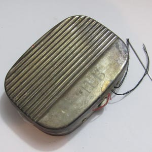 Puede incluir: Un kit de costura de metal vintage con una parte superior acanalada y las iniciales "ILB" grabadas en la superficie. El kit es rectangular con bordes redondeados e incluye una aguja e hilo.