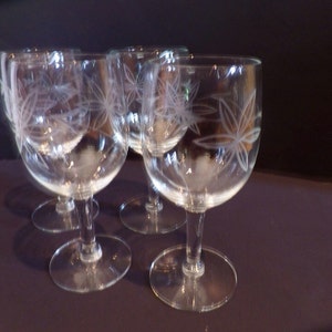 May include: Set of four clear glass wine glasses with etched floral designs. The glasses have a round bowl and a long stem.