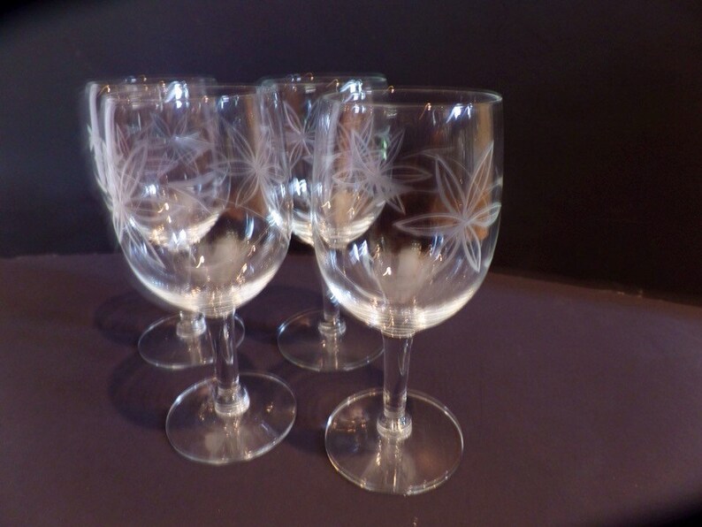 May include: Set of four clear glass wine glasses with etched floral designs. The glasses have a round bowl and a long stem.