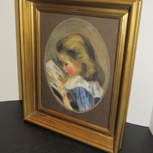 May include: A framed painting of a young girl with blonde hair reading a book. The painting is in an oval shape and is set against a brown background. The frame is gold.