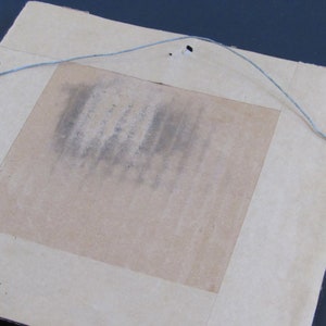 May include: The back of a framed picture with a brown cardboard backing and a wire hanger attached with metal eyelets.