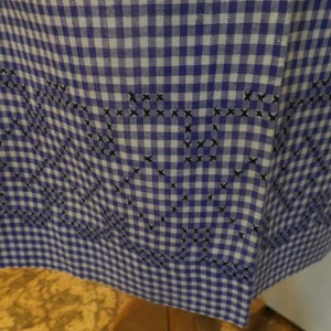 May include: A blue and white gingham fabric with a black embroidered design. The embroidery is in the shape of hearts and swirls.