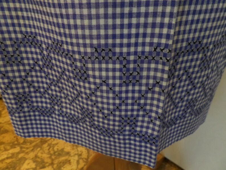 May include: A blue and white gingham fabric with a black embroidered design. The embroidery is in the shape of hearts and swirls.