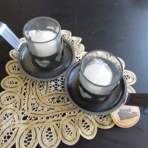 May include: Two black metal candle holders with a handle and a heart-shaped cutout. Each holder has a clear glass votive candle inside.
