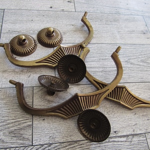 Puede incluir: Un surtido de tiradores y pomos de cajón de latón antiguo. Los tiradores tienen un diseño curvo con un patrón decorativo en forma de abanico. Los pomos son redondos con una superficie detallada y acanalada. La ferretería es de color latón envejecido.