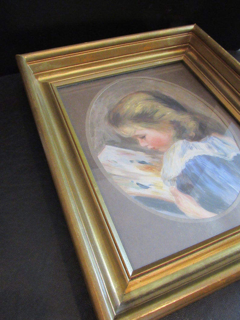 May include: A framed painting of a young girl reading a book. The painting is in a gold frame and the girl is wearing a blue dress with a white collar.