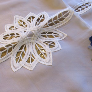 May include: White lace tablecloth with a delicate floral design. The lace is cut out in the shape of leaves and has a gold underlay. The tablecloth is made of a sheer fabric and has a light blue background.