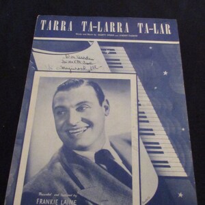 May include: A vintage sheet music cover for the song "Tarra Ta-Larra Ta-Lar" by Marty Symes and Johnny Farrow. The cover features a black and white photo of Frankie Laine, a popular singer from the 1940s and 1950s, with a signature in the top left corner. The cover is blue with white stars and a stylized piano.