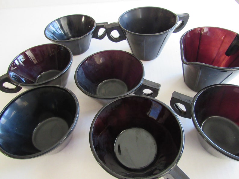 May include: Set of eight black and burgundy glass cups with handles. The cups are all the same size and shape, and they have a smooth, glossy finish.