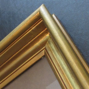 May include: Close-up of the corner of a gold picture frame with a raised, ornate design.