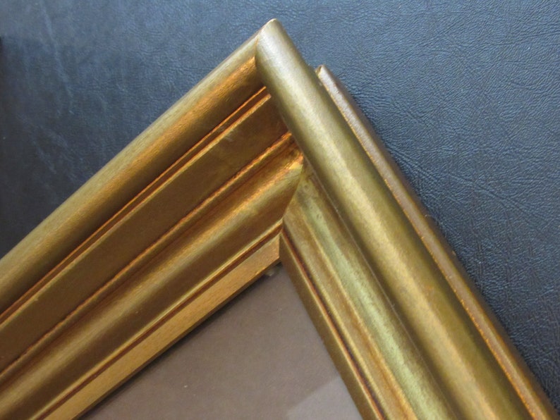 May include: Close-up of the corner of a gold picture frame with a raised, ornate design.