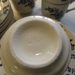 May include: Close-up of the underside of a white ceramic saucer with a blue floral design. The saucer has the word "USA" printed on the bottom.