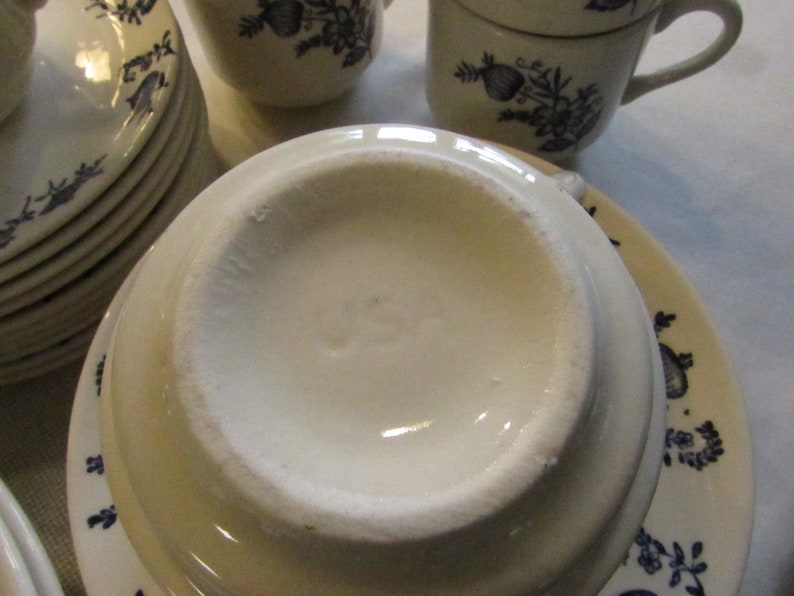 May include: Close-up of the underside of a white ceramic saucer with a blue floral design. The saucer has the word "USA" printed on the bottom.