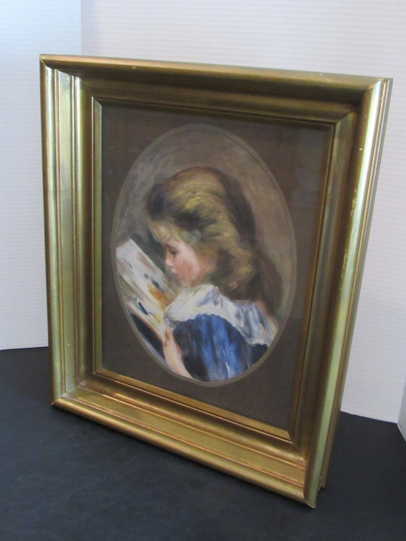 May include: A framed painting of a young girl in a blue dress reading a book. The painting is in an oval frame and is set against a brown background.