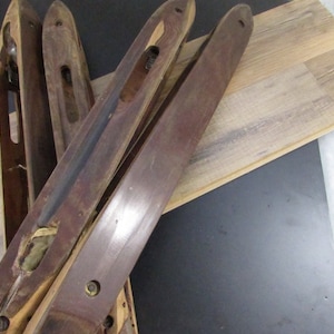 May include: Four wooden weaving shuttles with a dark brown finish. The shuttles are lying on a light brown wood surface.