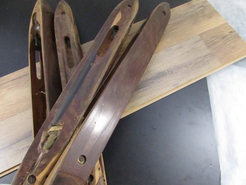 May include: Four wooden weaving shuttles with a dark brown finish. The shuttles are lying on a light brown wood surface.