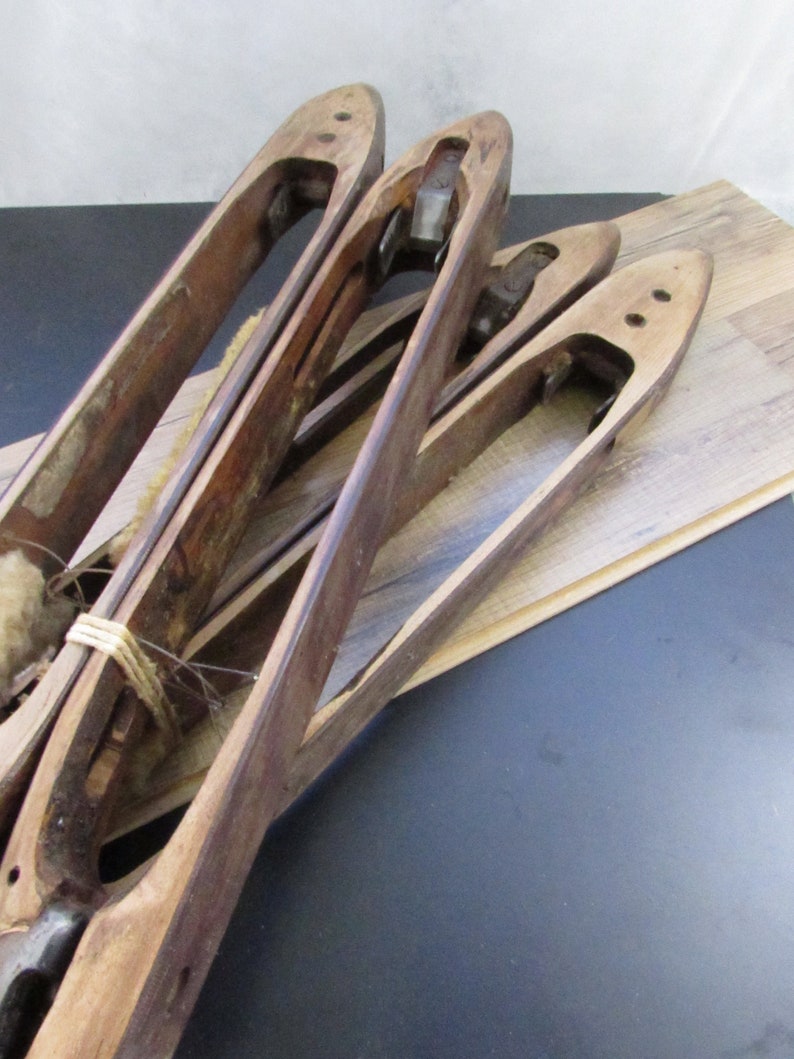May include: Four wooden weaving shuttles with metal parts. The shuttles are stacked on top of each other and are made of light brown wood.