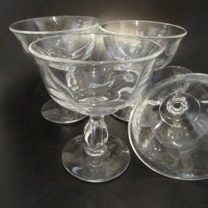 Puede incluir: Cuatro copas de postre de vidrio transparente con un diseño acanalado y un tallo corto. Las copas están dispuestas en grupo sobre una superficie negra.