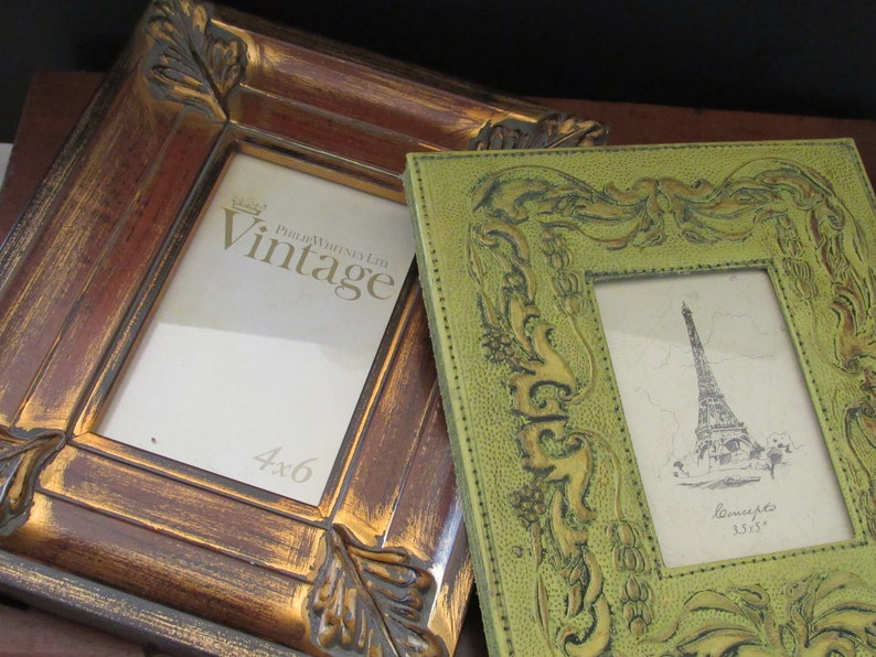 K&ouml;nnte beinhalten: Zwei Bilderrahmen, einer braun mit goldenen Akzenten und der andere gr&uuml;n mit gepr&auml;gten floralen Details. Der braune Rahmen tr&auml;gt den Text "Vintage" und "4x6". Der gr&uuml;ne Rahmen tr&auml;gt den Text "Reminiscents 3.5x5".