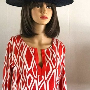 May include: A woman wearing a red and white geometric print dress with a wide-brimmed navy blue hat.