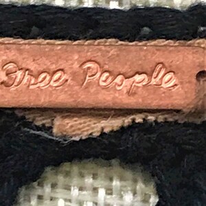 May include: Close-up of a brown leather tag with the text "Free People" embossed in gold lettering.