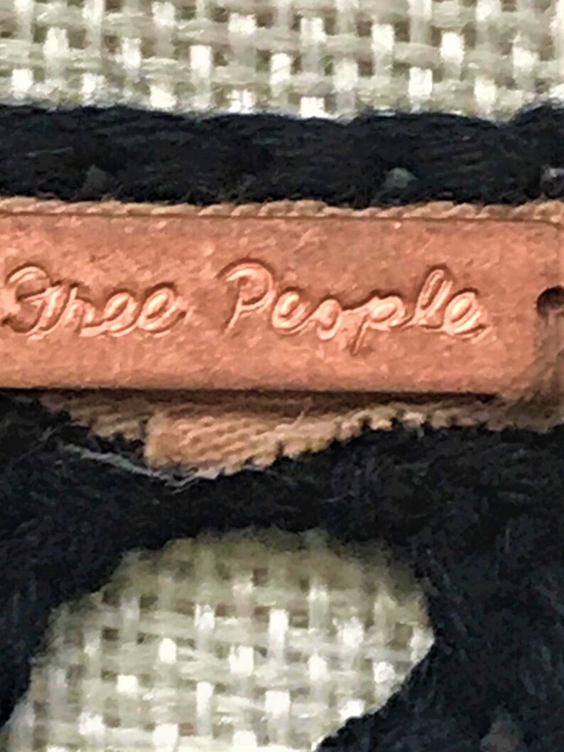 May include: Close-up of a brown leather tag with the text "Free People" embossed in gold lettering.