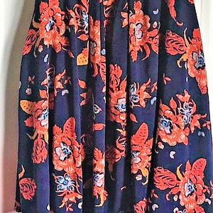 May include: A navy blue skirt with a floral print featuring red, orange, and white flowers. The skirt has a pleated design and a fitted waist.
