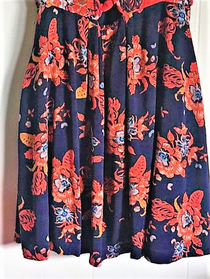 May include: A navy blue skirt with a floral print featuring red, orange, and white flowers. The skirt has a pleated design and a fitted waist.