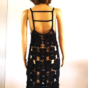 May include: Black crochet dress with a criss-cross strap detail on the back. The dress is made of a delicate, open-weave fabric and has a flowy, feminine silhouette.