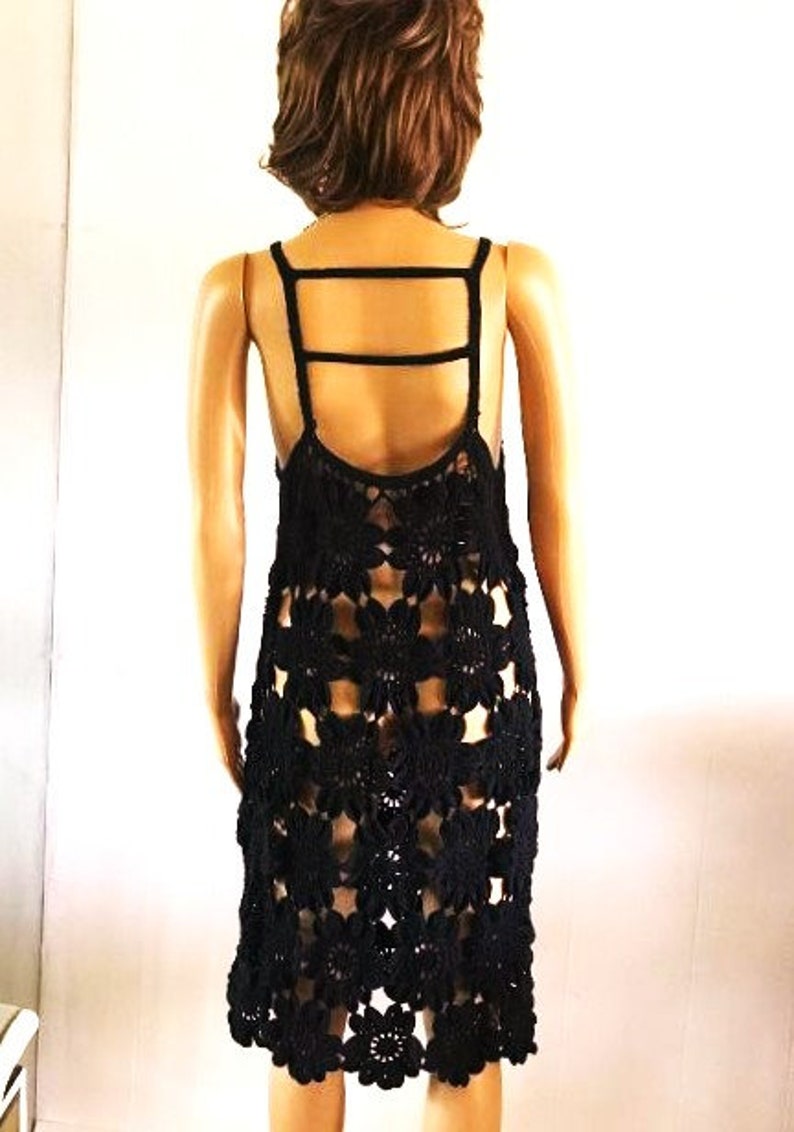 May include: Black crochet dress with a criss-cross strap detail on the back. The dress is made of a delicate, open-weave fabric and has a flowy, feminine silhouette.