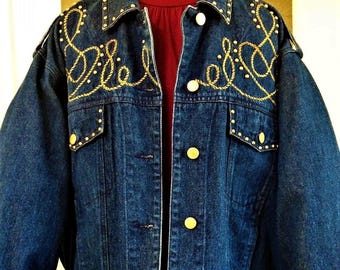 May include: A dark blue denim jacket featuring gold-toned metal buttons and intricate gold rope-style embroidery across the chest and collar. The jacket includes two chest pockets with buttoned flaps and is worn over a solid dark red turtleneck top.