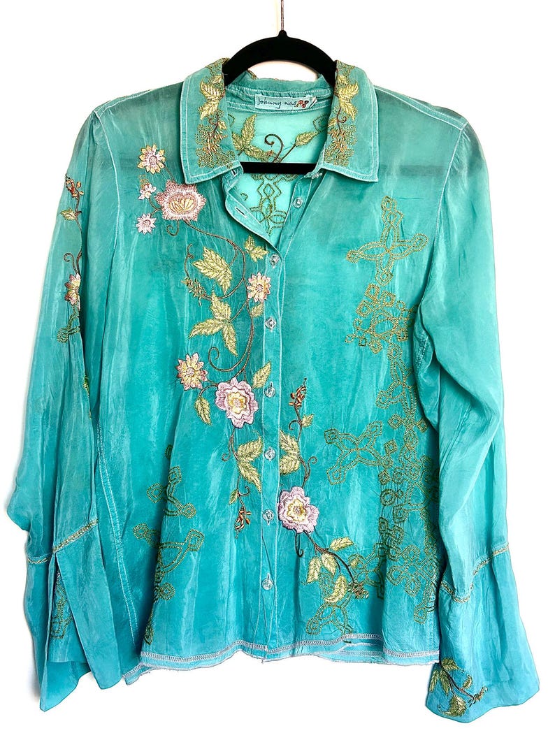 May include: A long-sleeved button-down shirt in a vibrant turquoise hue, featuring intricate gold thread embroidery and delicate pink floral accents. The garment includes a classic collar, a front button placket, and flared cuffs, showcasing detailed needlework across the front panels and collar.