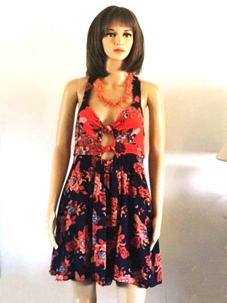 May include: A sleeveless floral dress with a red and black floral print. The dress has a halter neckline and a tie at the waist. The dress is made of a lightweight fabric and is perfect for summer.