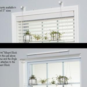 May include: A white window with white blinds and a shelf hanging above it. The shelf is supported by two white brackets attached to the wall. The shelf is holding two small plants. The text "Extension Mounts available in 2.5" and 5" sizes" is visible above the window. The text "The "No Trim" Mount Block installs on the wall above your window and the Angle Bracket attaches to the Mount Block" is visible below the window.