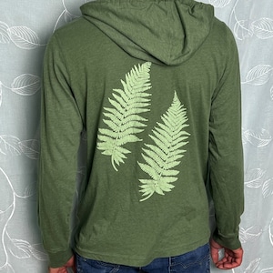 Puede incluir: Una sudadera con capucha verde de manga larga con un estampado de helecho en la espalda.