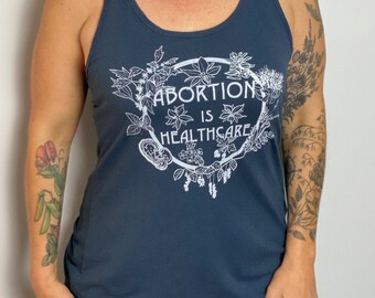 Puede incluir: Un top de tirantes azul oscuro con un diseño floral blanco y el texto "El aborto es atención médica".