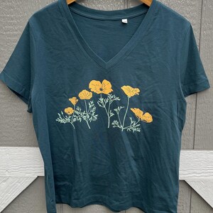 Puede incluir: Una camiseta azul turquesa de cuello en V con un estampado gr&aacute;fico de amapolas amarillas de California.