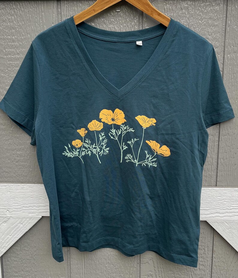 Puede incluir: Una camiseta azul turquesa de cuello en V con un estampado gr&aacute;fico de amapolas amarillas de California.