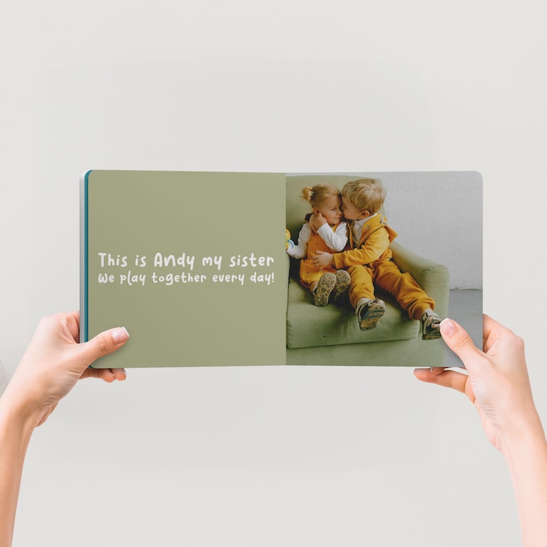 May include: A photo book held open, displaying a picture of two children hugging. The left page has the text "This is Andy my sister We play together every day!" in white. The book has a teal spine and a light green cover.