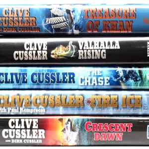 May include: A stack of five paperback books by Clive Cussler, featuring titles like "Treasure of Khan", "Valhalla Rising", "The Chase", "Fire Ice", and "Crescent Dawn".
