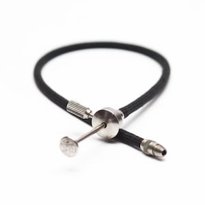 May include: A black flexible tube with a metal tip and a metal knob at the end. The tube is coiled and the metal tip is pointing towards the camera.