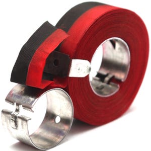 May include: A roll of red ribbon with a black and red ribbon strip, held in place by a metal ring and a metal ribbon cutter. The ribbon is tightly wound, and the cutter is attached to the roll.