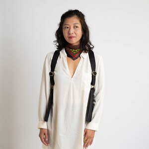 May include: A woman wearing a white shirt with a black and gold camera strap and a colourful patterned scarf around her neck.