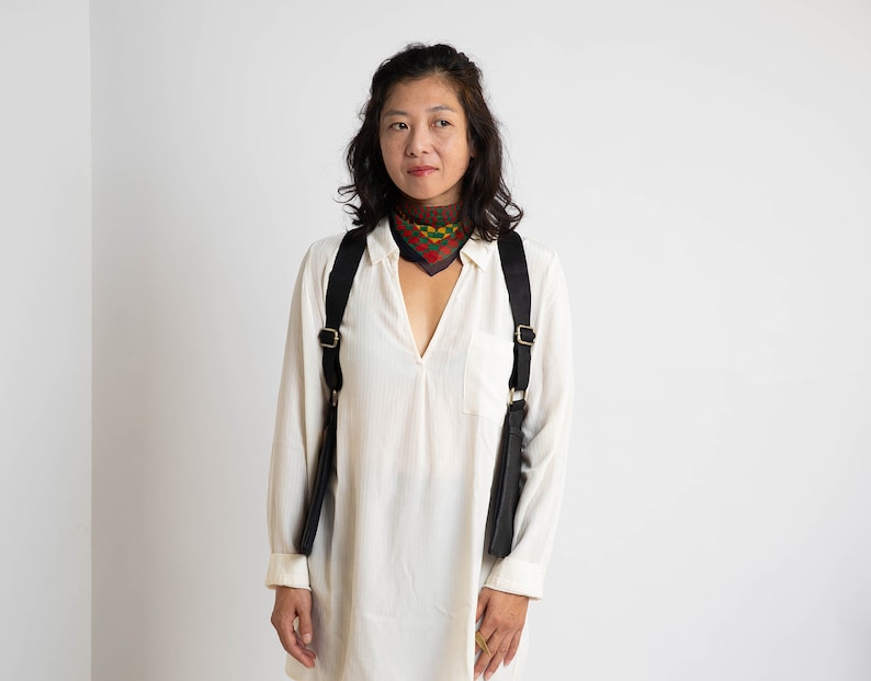 May include: A woman wearing a white shirt with a black and gold camera strap and a colourful patterned scarf around her neck.