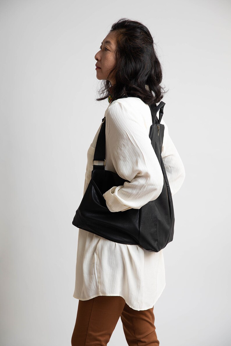 May include: A woman wearing a white shirt and brown trousers is carrying a black leather rucksack.