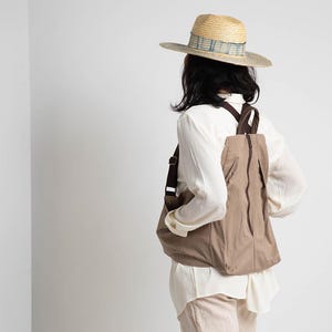 Puede incluir: Una persona con una camisa blanca y una mochila marr&oacute;n con un sombrero de paja. El sombrero tiene una banda con estampado azul y blanco.