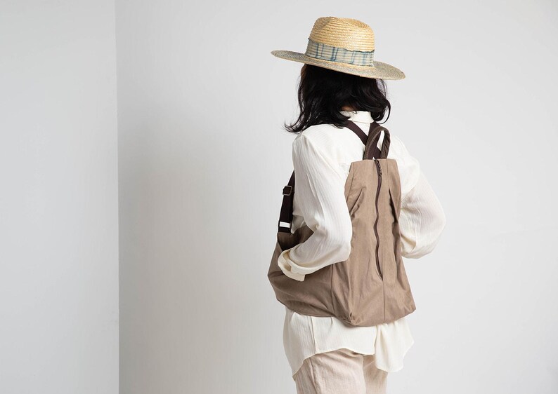 Puede incluir: Una persona con una camisa blanca y una mochila marr&oacute;n con un sombrero de paja. El sombrero tiene una banda con estampado azul y blanco.