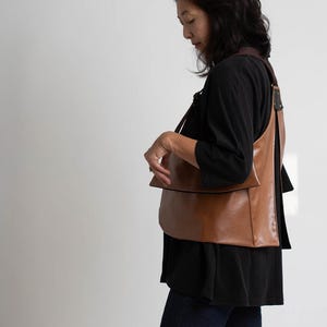 Puede incluir: Un bolso de hombro de cuero marr&oacute;n con una correa ancha. El bolso tiene un dise&ntilde;o simple y minimalista y parece estar hecho de cuero liso. El bolso se lleva sobre el hombro.