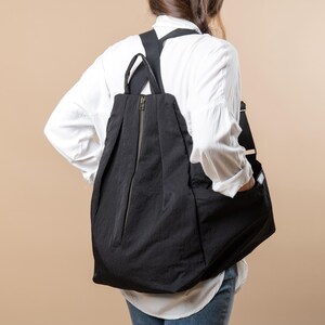 Puede incluir: Una persona con una camisa blanca y una mochila negra. La mochila tiene una cremallera y una solapa.